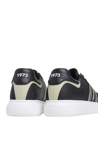 Schwarze Ledersneaker mit kontrastierenden hellbraunen Akzenten, einer weißen Sohle und der Prägung "1973" an der Ferse. Besitzt zwei weiße Streifen an der Seite.