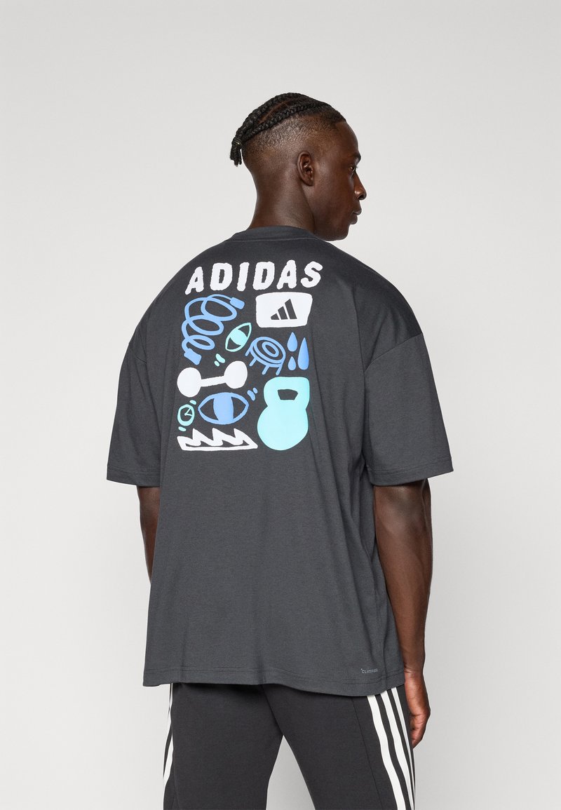 Lyhythihainen, tummanharmaa puuvillapaita, jossa on värikkäitä graafisia kuvastoja ja 'ADIDAS' -teksti painettuna taakse.