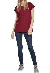 Burgundské tričko s krátkým rukávem v kombinaci s tmavými skinny džínami a šedými vysokými sneakers. Měkká látka, uvolněný střih, minimální detaily.