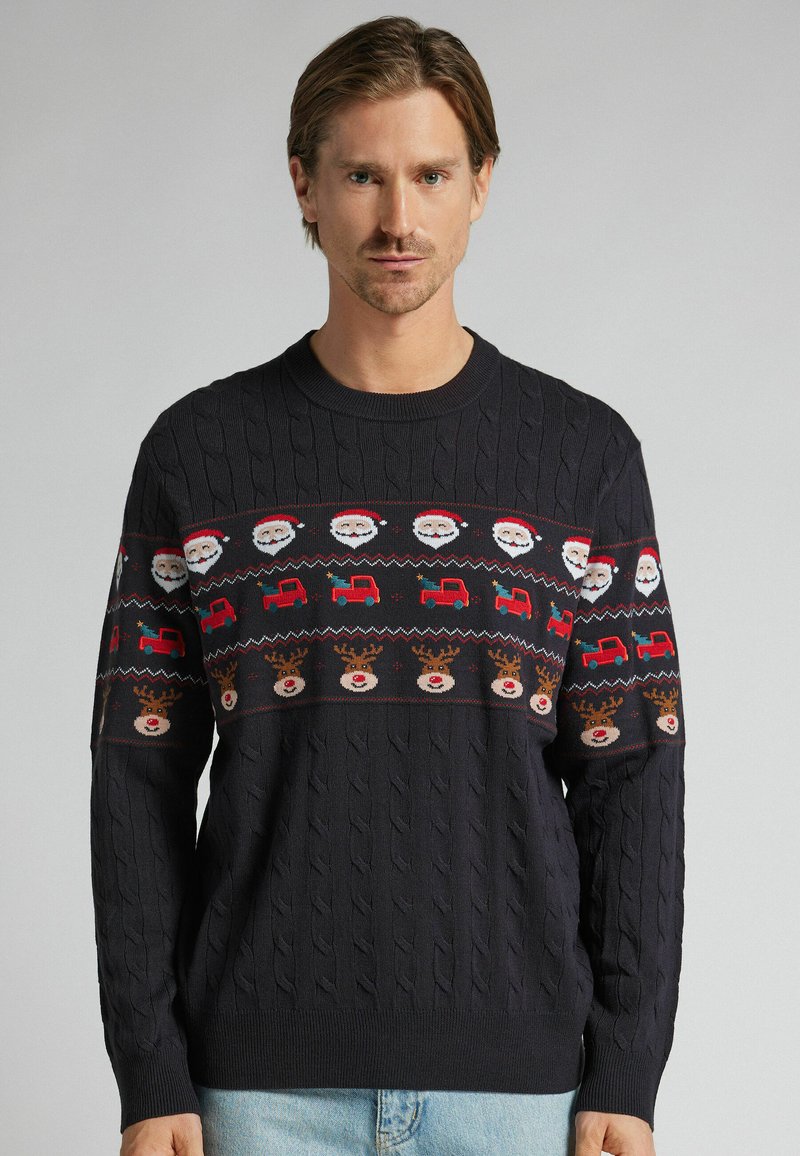 Granatowy sweter z dzianiny z świątecznym wzorem przedstawiającym twarze Świętego Mikołaja, czerwone ciężarówki i renifery. Wzór warkocza na ciele i rękawach.