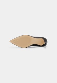 Chaussure à talon haut noire à bout pointu vue de la semelle, présentant une semelle beige avec la marque "GUESS" et la taille 40.