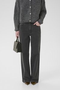 Zwarte wijde jeans met hoge taille, gecombineerd met een grijze gemêleerde cardigan en puntige schoenen, terwijl ze een kleine zwarte handtas vasthoudt.
