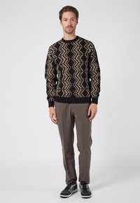 Maglione nero con un motivo a zigzag beige. Abbinato a pantaloni marroni con texture e sneakers neri. Design semplice con colletto rotondo.