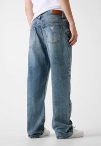 Jasnoniebieskie dżinsy w stylu denim o luźnym kroju, z naszywką z skóry na pasku oraz trójkątnym logo na tylnej kieszeni.