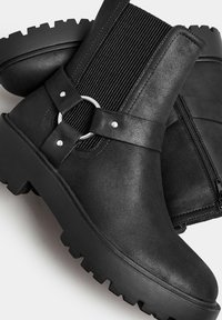 Black ankle boots featuring a textured matte finish, elastic side panels, a metal ring accent, and a chunky, ridged rubber sole.