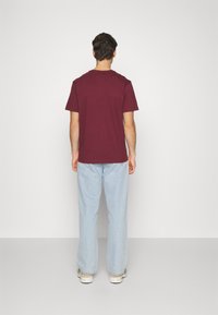 Camiseta de manga corta color burdeos, de algodón, con un ajuste holgado, combinada con unos jeans de pierna ancha azul claro, ambos con detalles mínimos.