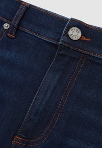 Tmavě modré džíny z denimu s oranžovým prošíváním, zapnutým horním knoflíkem a detailem poutka na pásek na pásu.