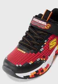 Red and black sneakers feature a pixelated design with orange, gray, and white accents, black laces, and a Velcro strap with branding.