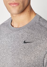 Graues Sport-T-Shirt aus strukturiertem Stoff, mit einem schwarzen Nike-Logo auf der Brust und einem runden Halsausschnitt.