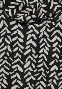 Černá pletenina s abstraktním krémovým vzorem různých tvarů, včetně křivek a šipek, vytvářející texturovaný design.