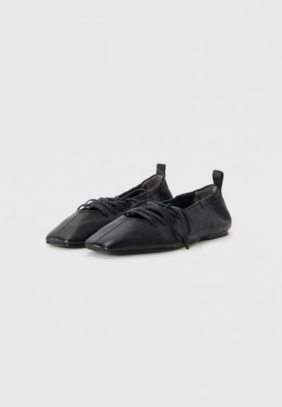 Chaussures en cuir noir avec un design à bout pointu, fermeture à lacets et une finition élégante, présentant un petit talon et des détails de couture minimalistes.