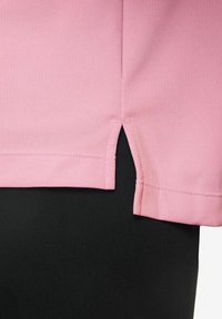 T-shirt rosa con una texture morbida, caratterizzata da un taglio dritto e fessure laterali. Posizionata sopra un tessuto nero, mette in evidenza il contrasto di colore.