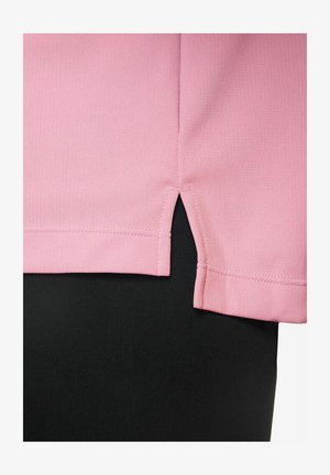 Camiseta rosa con una textura suave, que presenta un corte recto y aberturas laterales. Colocada sobre una tela negra, resaltando el contraste de colores.