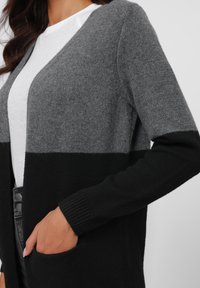 Knitted cardigan featuring a color-block design in dark gray, light gray, and black. Long sleeves with ribbed cuffs and side pockets.
