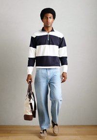 Pullover a righe blu navy e bianche con collo a mezza zip, abbinato a jeans azzurri. Porta una borsa bicolore con una texture morbida.
