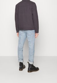 Sort lærredjakke med krave, lyseblå jeans og sorte snørebukser med platformsål, set bagfra.