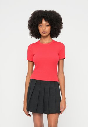 Top rosso a maniche corte con costine e scollo rotondo abbinato a una gonna nera plissettata, caratterizzata da una texture liscia e un design strutturato.