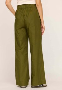 Pantalons larges vert olive avec une taille élastique, présentant une texture lisse et un design décontracté. Coupe standard à la cheville.