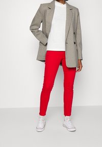 Szary żakiet w wzór houndstooth, biały top i jasnoczerwone skinny jeans w połączeniu z białymi trampkami. Żakiet ma dwa z przodu guziki i luźny krój.