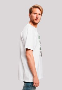 White cotton t-shirt with a crew neck, short sleeves, and graphic print featuring green text and forest imagery. Loose fit.