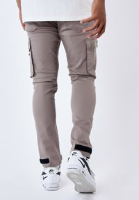 Pantalones cargo beige con un ajuste slim, bolsillos laterales y un diseño de pierna ajustada. Combinados con zapatillas Nike blancas con acentos negros.