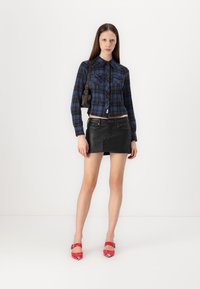 Blue and black plaid cropped shirt, black leather miniskirt, red high-heeled shoes with silver accents, and a small shoulder bag.