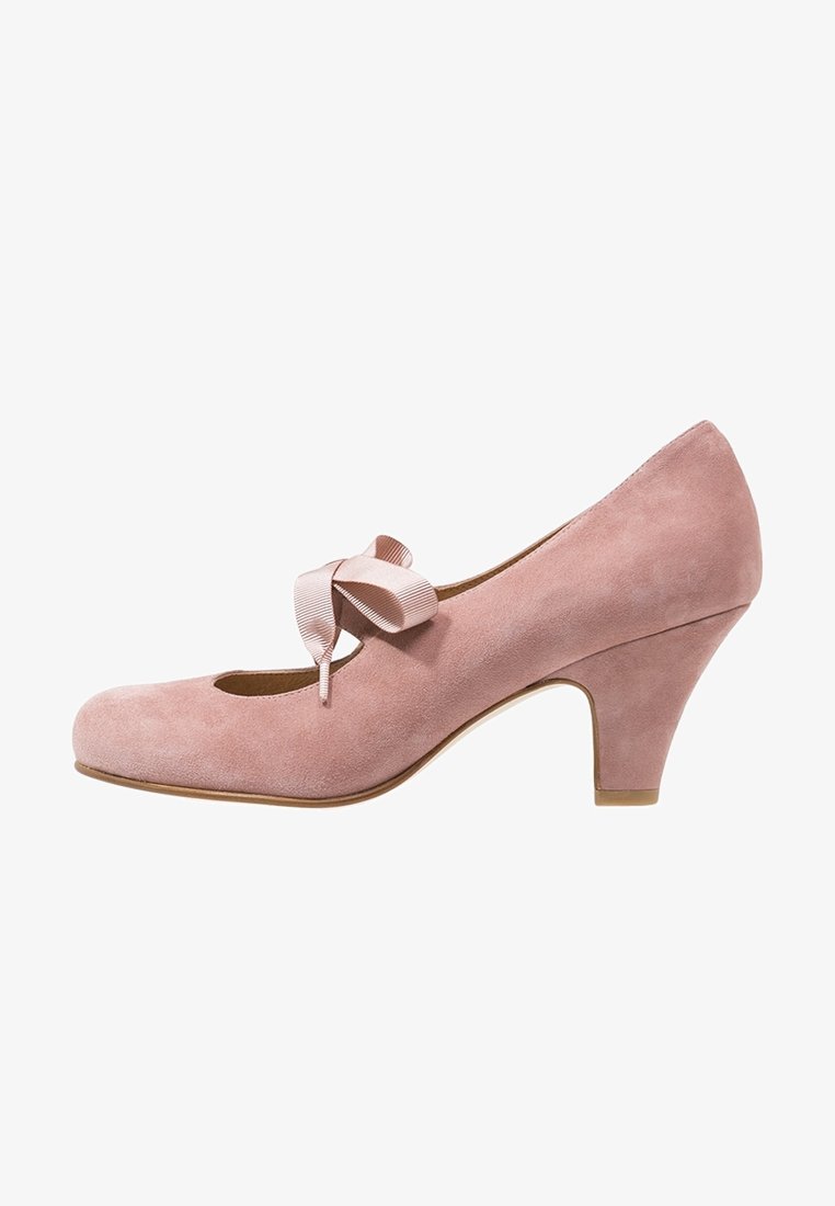 Chaussure à talon haut en daim rose avec un bout arrondi et un nœud en satin décoratif sur le côté. Elle présente une surface légèrement texturée et un talon modéré.