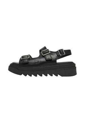 Sandalias negras de cuero con correas de hebilla doble, suela gruesa y estriada, y diseño de punta abierta. Detalles texturizados realzan el aspecto general.