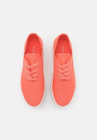 Koralowe tenisówki z tkaniny z sznurowaniem, posiadające zaokrąglony nosek i jasnokolorową gumową podeszwę. Gładka faktura z minimalistycznymi akcentami.