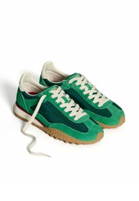 Zapatillas de gamuza verde con un diseño texturizado, cordones crema y una suela de goma con una franja de acento roja en el talón.