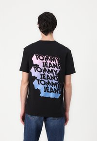 Sort bomulds t-shirt med multicoloreret "TOMMY JEANS" tekst på ryggen, med en gradient fra pink til blå. Korte ærmer, rund hals.