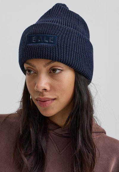 Jūras spēku adīts beanie ar ribotu tekstūru un taisnstūrveida uzlīmi, kurā ir vārds "BALL" tumši zilā krāsā. Ar norādītu augšpusi.