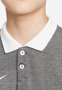 Grijze polo met een witte kraag, voorzien van een drieknopenrij en een wit Nike-logo aan de linkerkant. Zachte textuur.