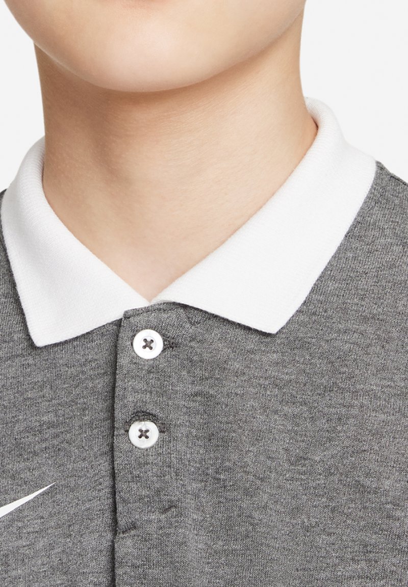 Grijze polo met een witte kraag, voorzien van een drieknopenrij en een wit Nike-logo aan de linkerkant. Zachte textuur.