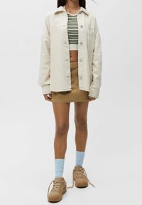Overdimensioneret cremefarvet kordfløjlskjorte med knapper, stribet crop top, tan mini nederdel, lyseblå sokker og beige sneakers. Diskret tekstur og lagdelt design.
