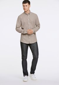 Camicia button-up marrone chiaro con maniche lunghe, abbinata a jeans blu scuro e sneakers bianche. La camicia presenta una sottile trama.
