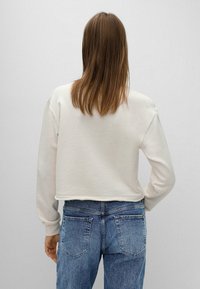 Sudadera de crema recortada con mangas ajustadas, combinada con jeans de cintura alta de color azul claro que presentan una textura desvanecida y bolsillos traseros.