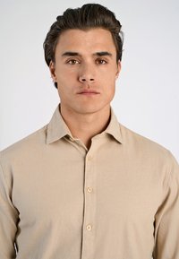 Camicia beige con bottoni, caratterizzata da una texture morbida, colletto a punta e dettagli di cucitura sottili lungo la chiusura e le maniche.