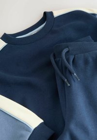 Zestaw granatowej bluzy i spodni dresowych wykonany z miękkiego materiału. Bluza ma jasnoniebieskie i kremowe akcenty, ściągacze oraz okrągły dekolt.