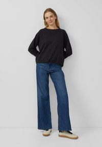 Zwarte trui met een ronde hals en elastische zoom, gecombineerd met blauw wijde pijpen spijkerbroek en crème sneakers met zwarte veters en een rubberen zool.