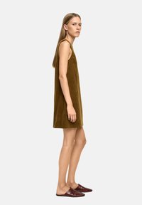 Sukienka bez rękawów, długości do kolan, w oliwkowozielonym kordie z prostym krojem. Połączona z bordowymi butami wsuwanymi.