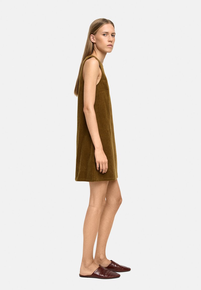 Sukienka bez rękawów, długości do kolan, w oliwkowozielonym kordie z prostym krojem. Połączona z bordowymi butami wsuwanymi.