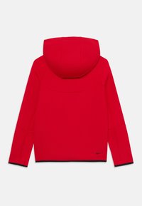 Giacca rossa con cappuccio in tessuto liscio. Presenta dettagli neri lungo l'orlo e le maniche. Logo Nike visibile sulla parte anteriore bassa.