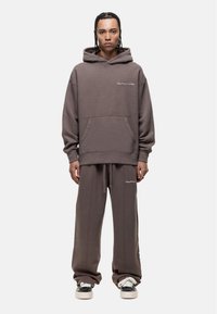 Brown hooded sweatshirt with a front pocket and embroidered logo, paired with matching sweatpants featuring side pockets and drawstring.