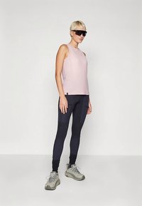 Top rosa chiaro senza maniche, leggings neri con texture diverse e scarpe sportive grigie. Occhiali da sole grandi neri completano il look.