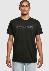 Sort bomulds T-shirt med "IRON MAIDEN" i flerfarvet, stiliseret skrift hen over brystet. Korte ærmer og runde halsudskæring.