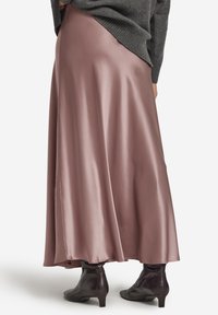 Lang, flydende satin nederdel i blød mauve med en glat tekstur, kombineret med tætsiddende, mørke læderankelstøvler. Klassisk A-linje silhuet.