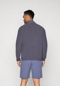 Φούτερ σε σκούρο γκρί με ψηλό γιακά, μακριά μανίκια και μία μικρή λεπτομέρεια στο πίσω μέρος, συνδυασμένο με ανοιχτό μπλε σορτς.