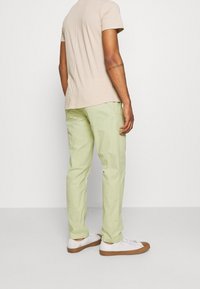 Light green cotton trousers with a relaxed fit, paired with white sneakers and a beige t-shirt, viewed from the back.