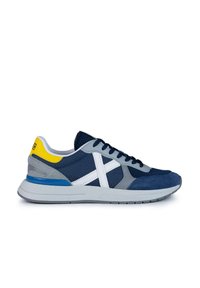 Zapatilla atlética azul marino con una combinación de materiales de malla y ante, que presenta acentos grises, un logo blanco y una lengüeta amarilla en el talón con detalles azules.